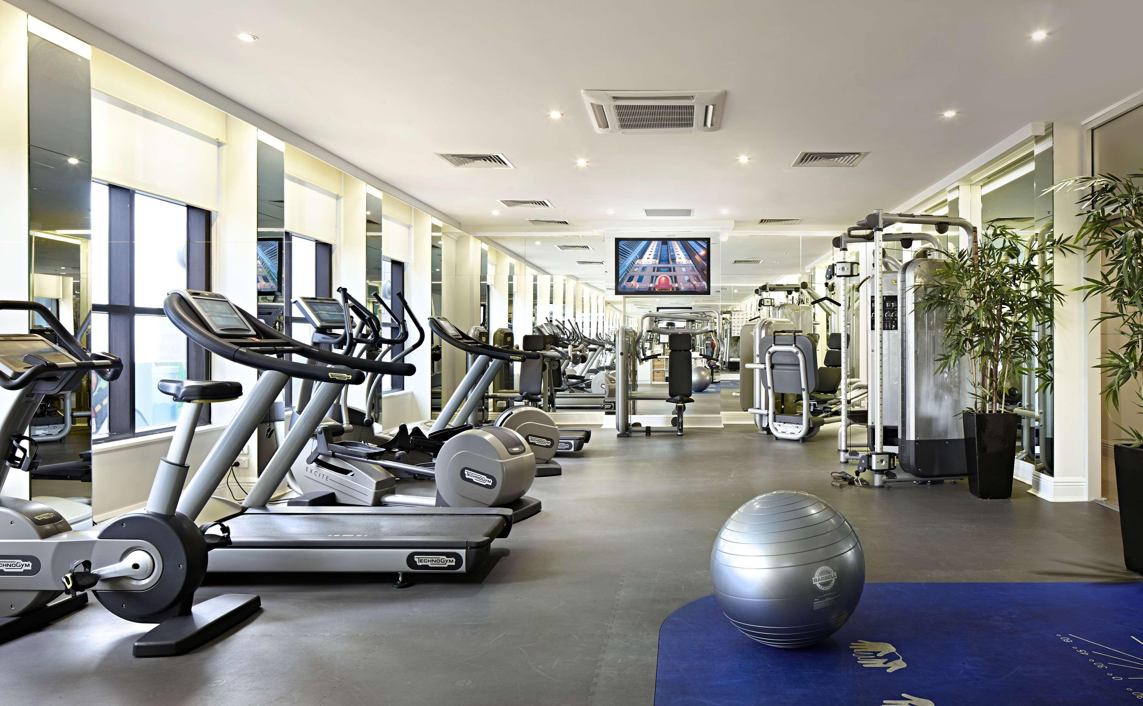Hotel Stamford Plaza Melbourne Zewnętrze zdjęcie The photo shows a modern gym or fitness center. There are several exercise machines, including treadmills and elliptical trainers, positioned near large windows that allow natural light to flood the space. A television is mounted on the wall, likely 