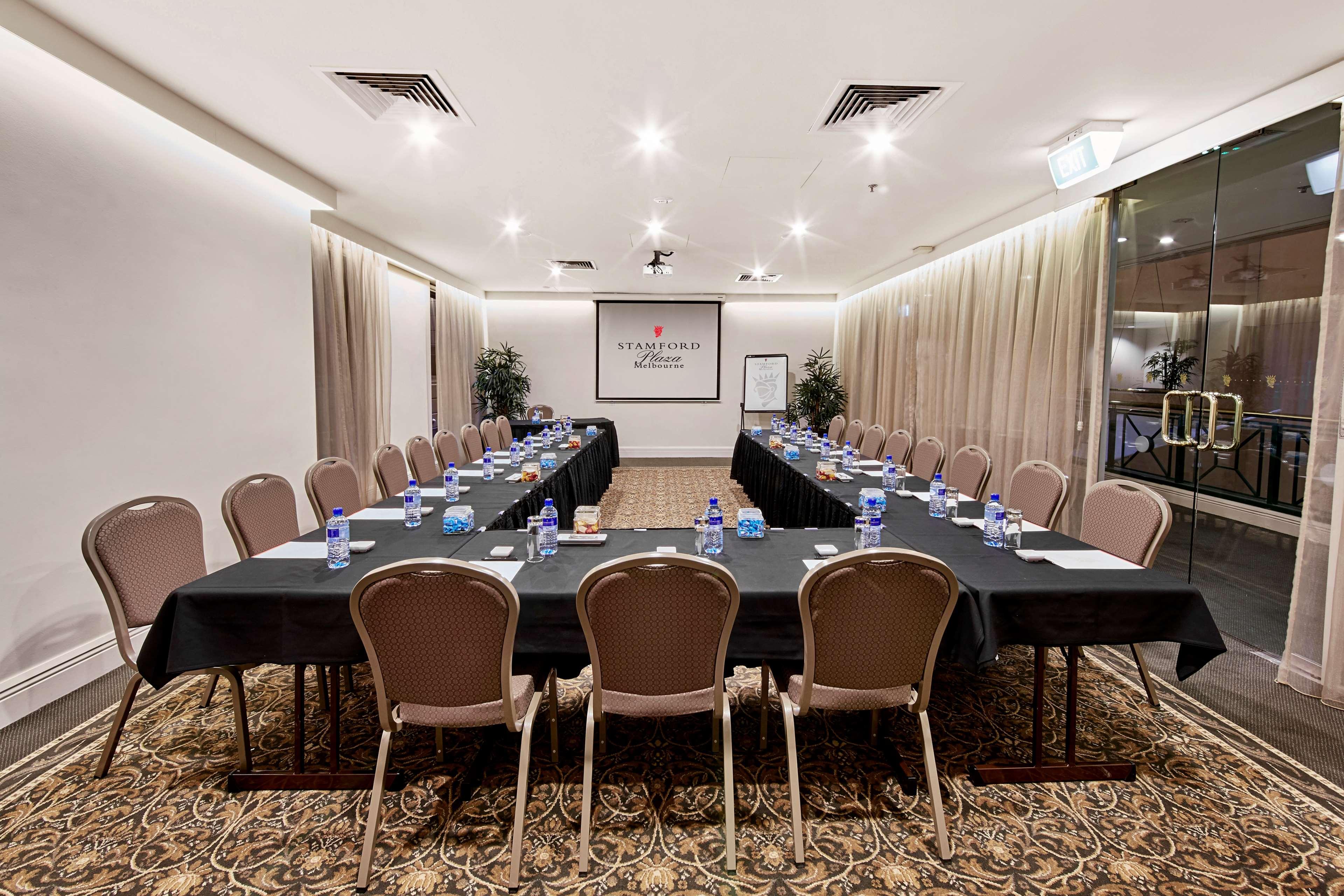 Hotel Stamford Plaza Melbourne Zewnętrze zdjęcie The photo shows a conference room set up for a meeting. There are several long tables arranged in a U-shape, covered with black tablecloths. Each table has a water bottle and notepad placed at intervals. The room is well-lit, with light-colored walls