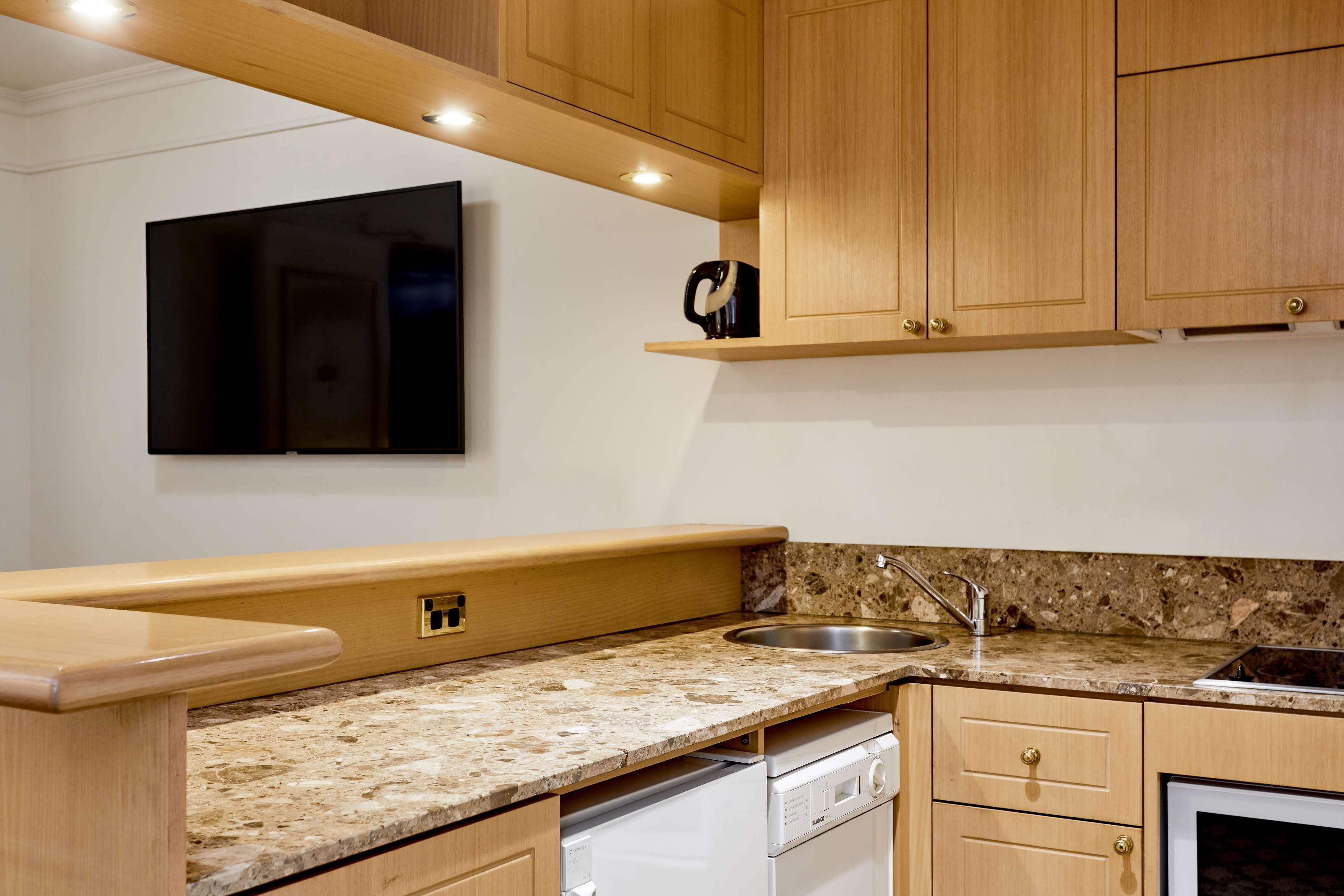 Hotel Stamford Plaza Melbourne Zewnętrze zdjęcie The photo shows a modern kitchen with wooden cabinetry and a granite countertop. There's a stainless steel sink integrated into the countertop, and appliances including a dishwasher and possibly a coffee maker on the shelf above. A flat-screen televi