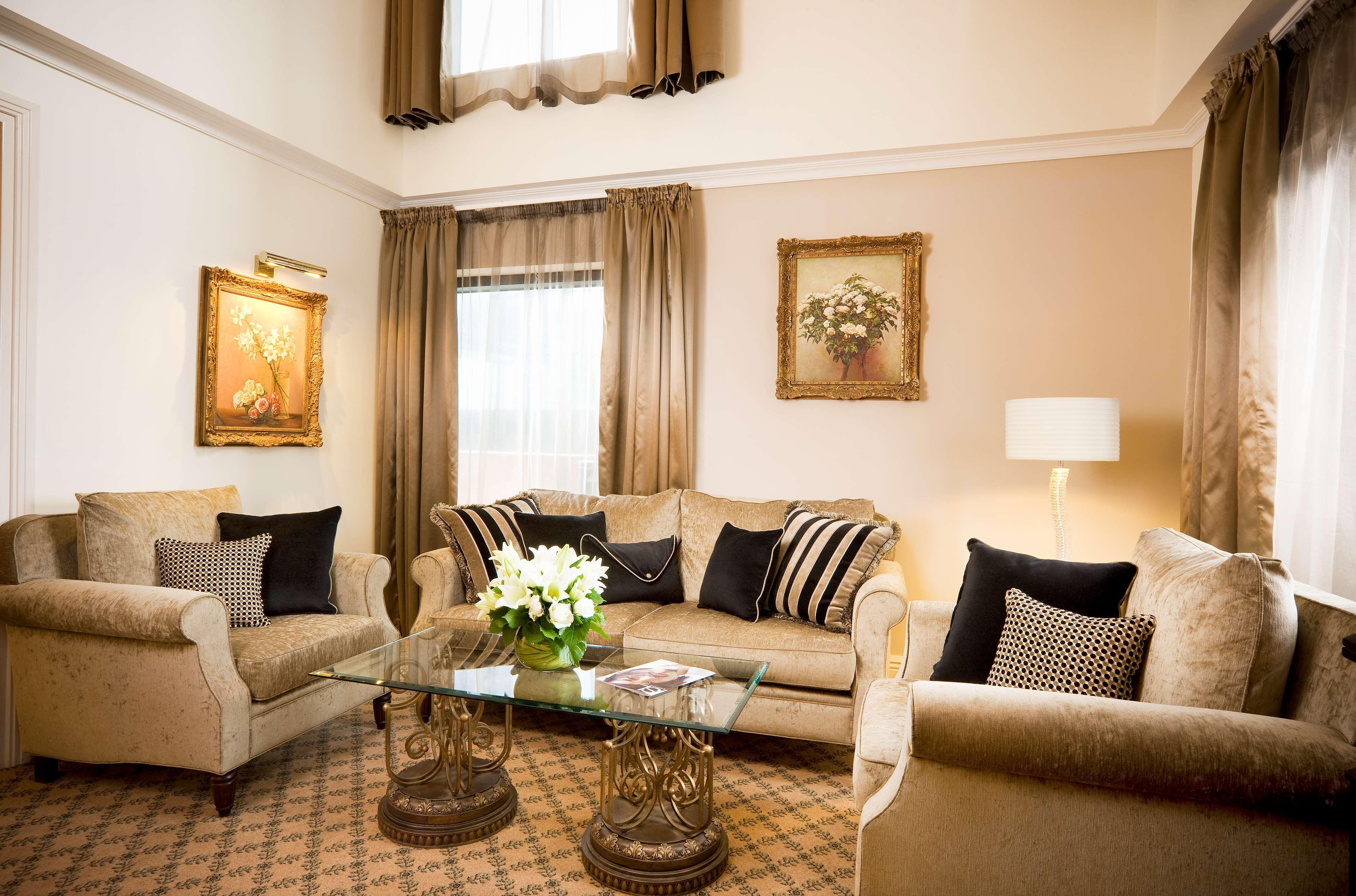 Hotel Stamford Plaza Melbourne Pokój zdjęcie The photo depicts a stylish living room with a warm and inviting aesthetic. It features a set of comfortable beige sofas adorned with decorative pillows in black and patterned designs. There is a glass coffee table at the center, supported by elegant