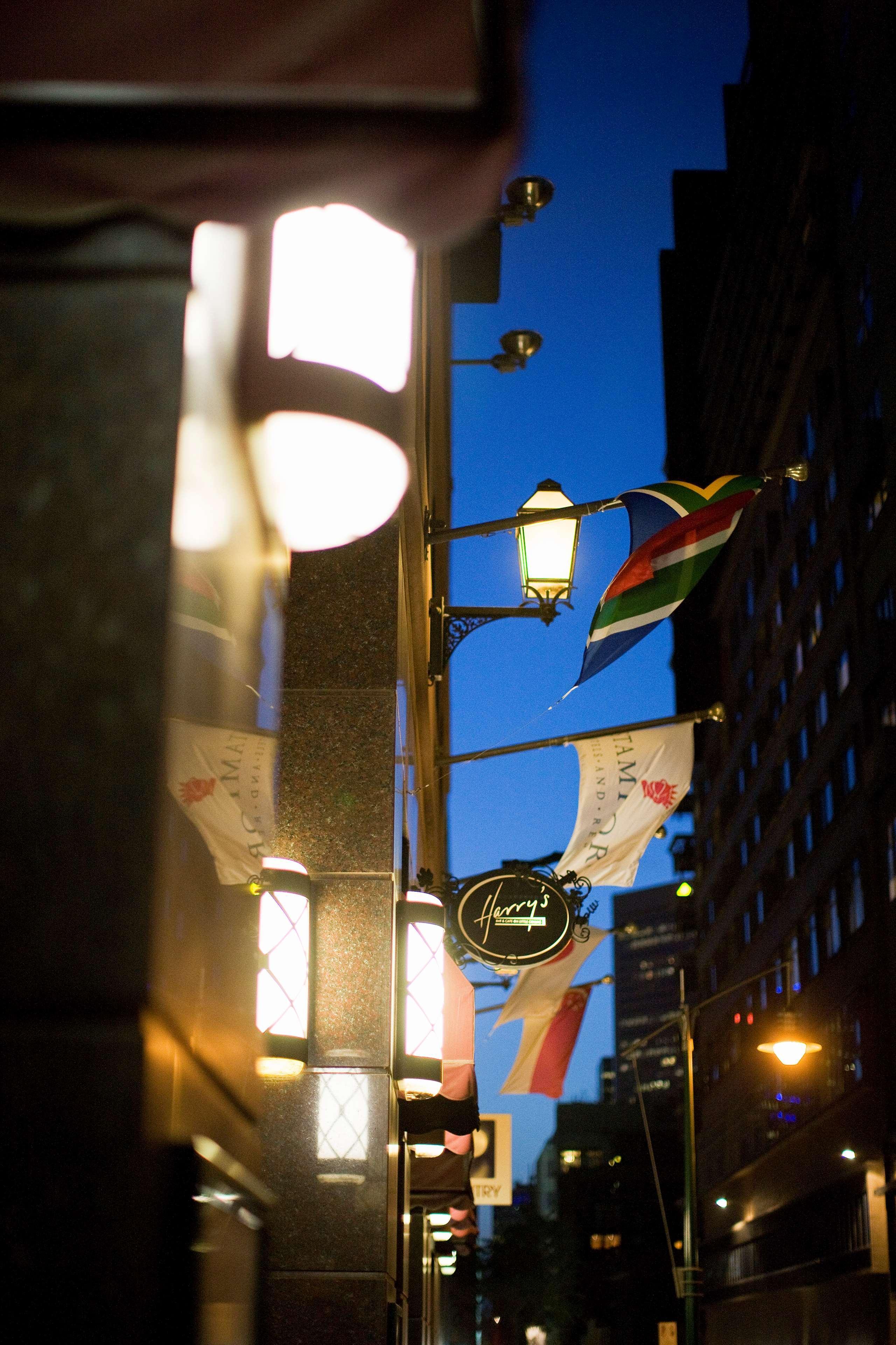 Hotel Stamford Plaza Melbourne Zewnętrze zdjęcie The photo features a street view of a building at dusk. Prominently displayed are several flags, including a South African flag, which are fluttering in the wind. There is a sign that reads "Harry's," likely indicating the name of a business or estab