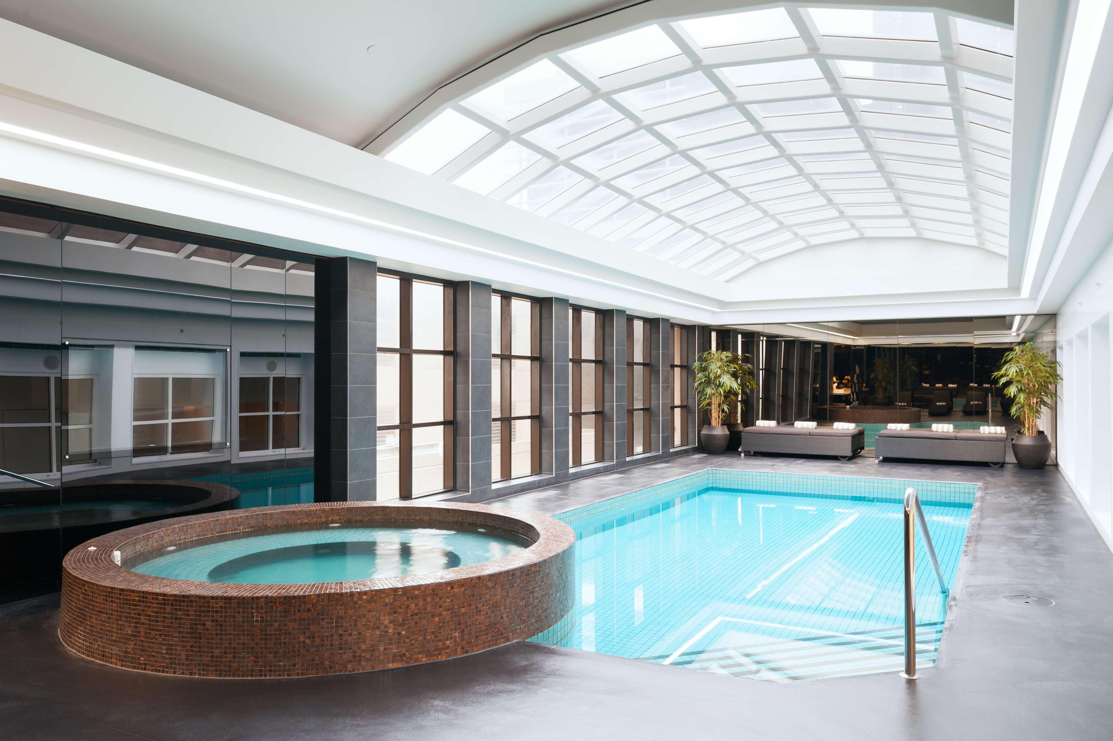 Hotel Stamford Plaza Melbourne Zewnętrze zdjęcie The photo shows an indoor swimming pool area. The pool is rectangular and has clear blue water, surrounded by a sleek, modern design. On one side, there is a round hot tub made of dark stone. Large windows line the walls, allowing natural light to fi