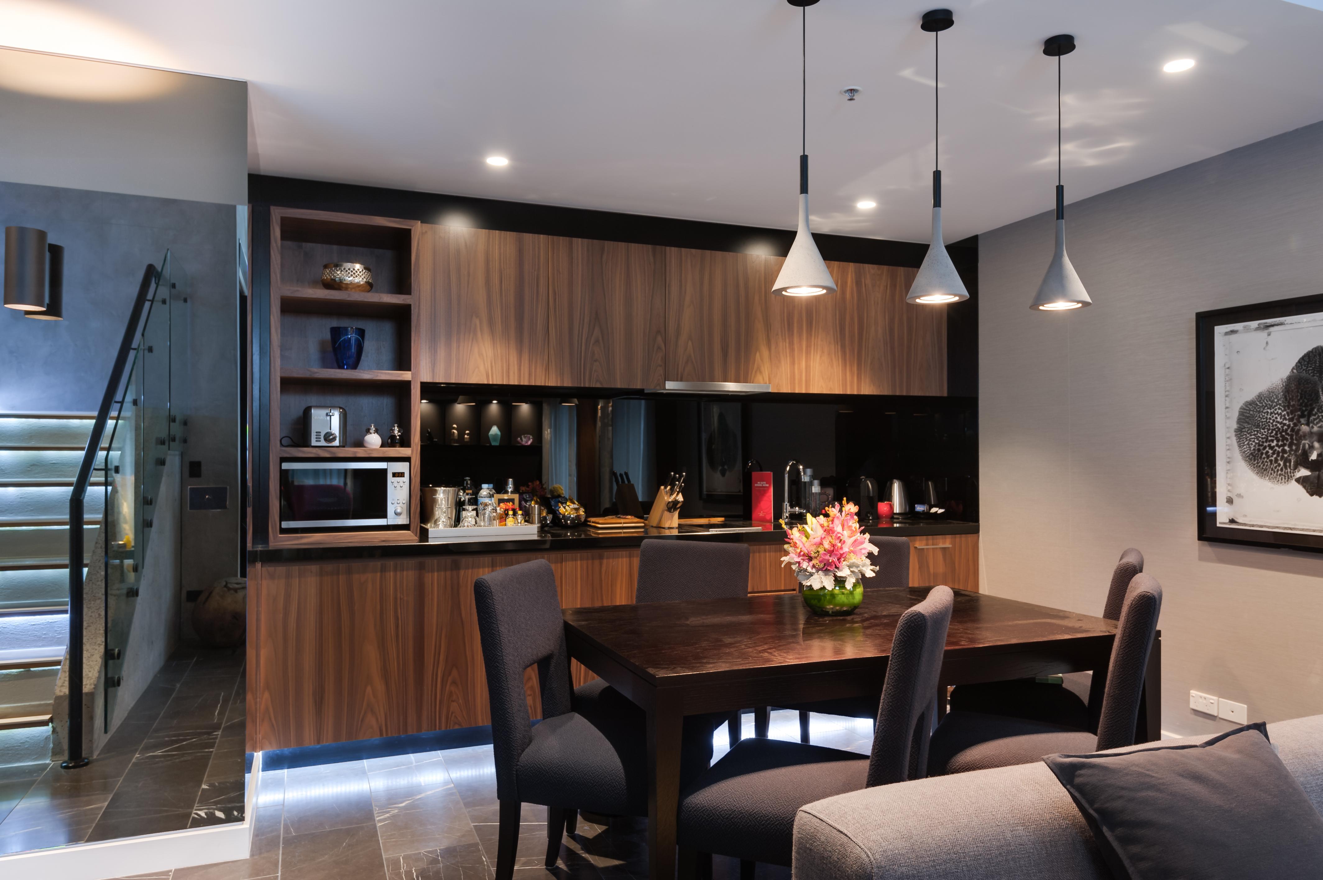 Hotel Stamford Plaza Melbourne Zewnętrze zdjęcie The image shows a modern kitchen and dining area. The kitchen features dark wooden cabinetry with black accents, a microwave, and various kitchen items arranged on the shelves. There is a dining table made of dark wood, surrounded by several chairs. 