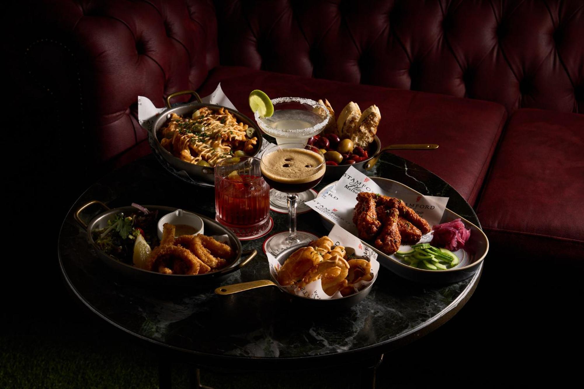 Hotel Stamford Plaza Melbourne Zewnętrze zdjęcie The photo showcases a variety of delicious foods and drinks arranged on a dark marble table. There are several dishes including:

1. A large bowl of pasta with a creamy sauce.
2. A platter of chicken wings, likely spicy or barbecued.
3. A small salad