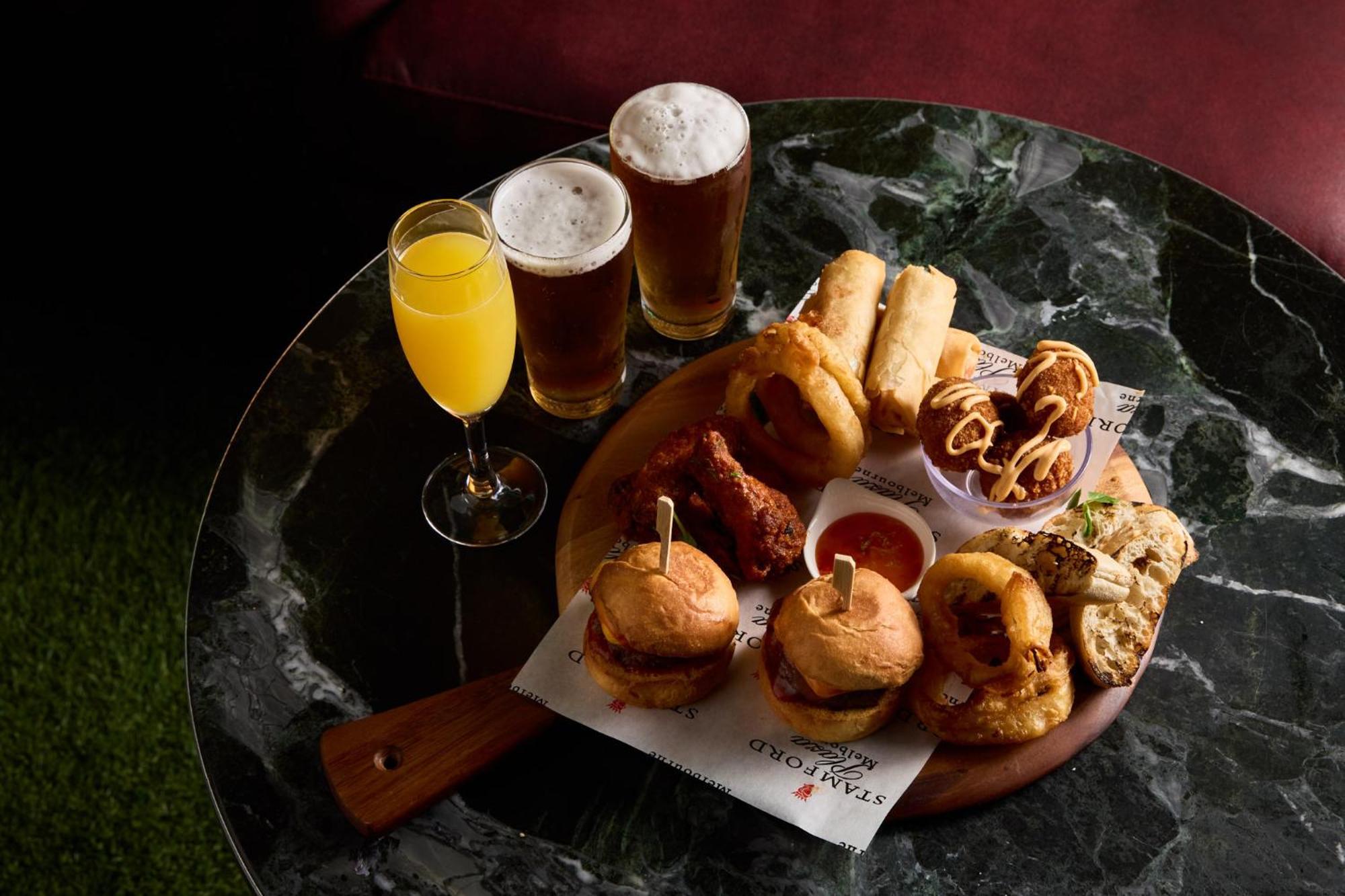 Hotel Stamford Plaza Melbourne Zewnętrze zdjęcie The photo displays a variety of food and drinks arranged on a marble table. There are small burgers garnished with skewers, crispy chicken pieces, and deep-fried snacks. Additionally, there are two glasses of beer and a cocktail, likely a mimosa, pre
