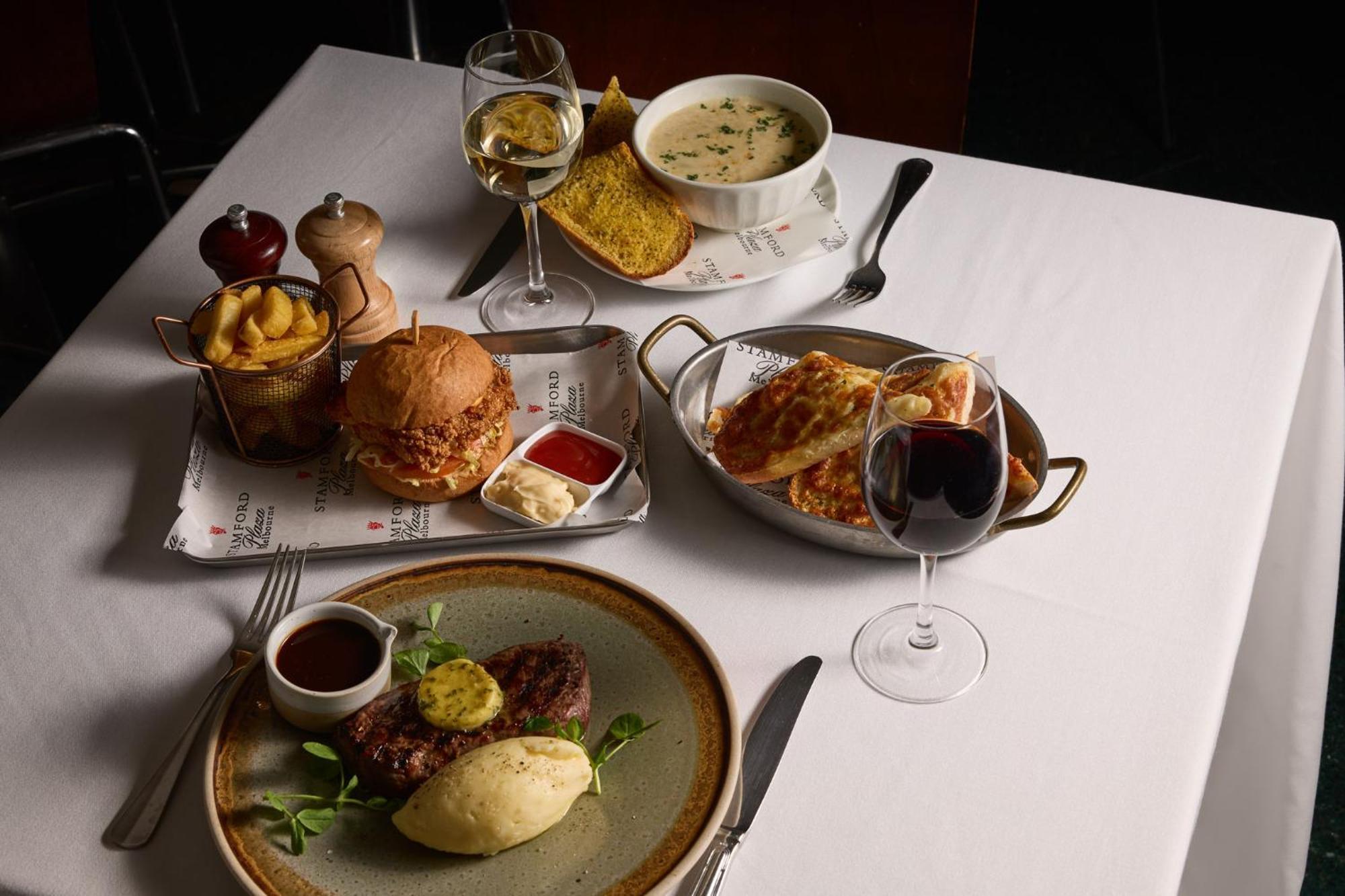 Hotel Stamford Plaza Melbourne Zewnętrze zdjęcie The photo showcases a variety of food and drinks arranged on a table set with a white tablecloth. 

1. **Main Dish:** A plate features a portion of steak topped with a slice of butter, accompanied by mashed potatoes and a garnish of greenery.
2. **Bu