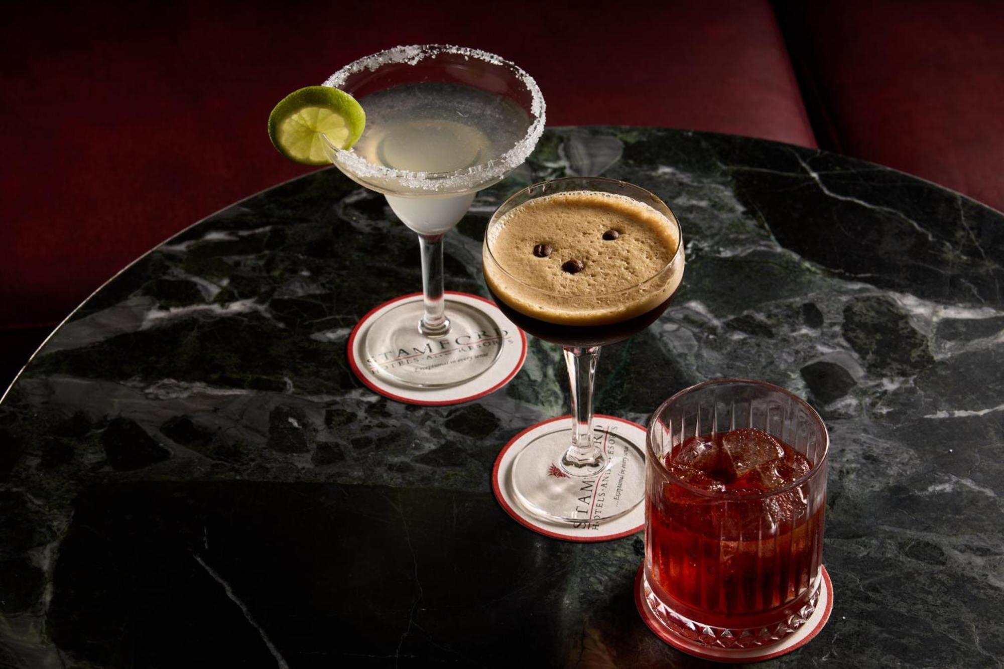 Hotel Stamford Plaza Melbourne Zewnętrze zdjęcie The photo features three different cocktails displayed on a dark, marble table. 

1. **Left Cocktail**: A margarita served in a traditional glass, garnished with a lime wedge and featuring a salted rim.
2. **Middle Cocktail**: An espresso martini in 