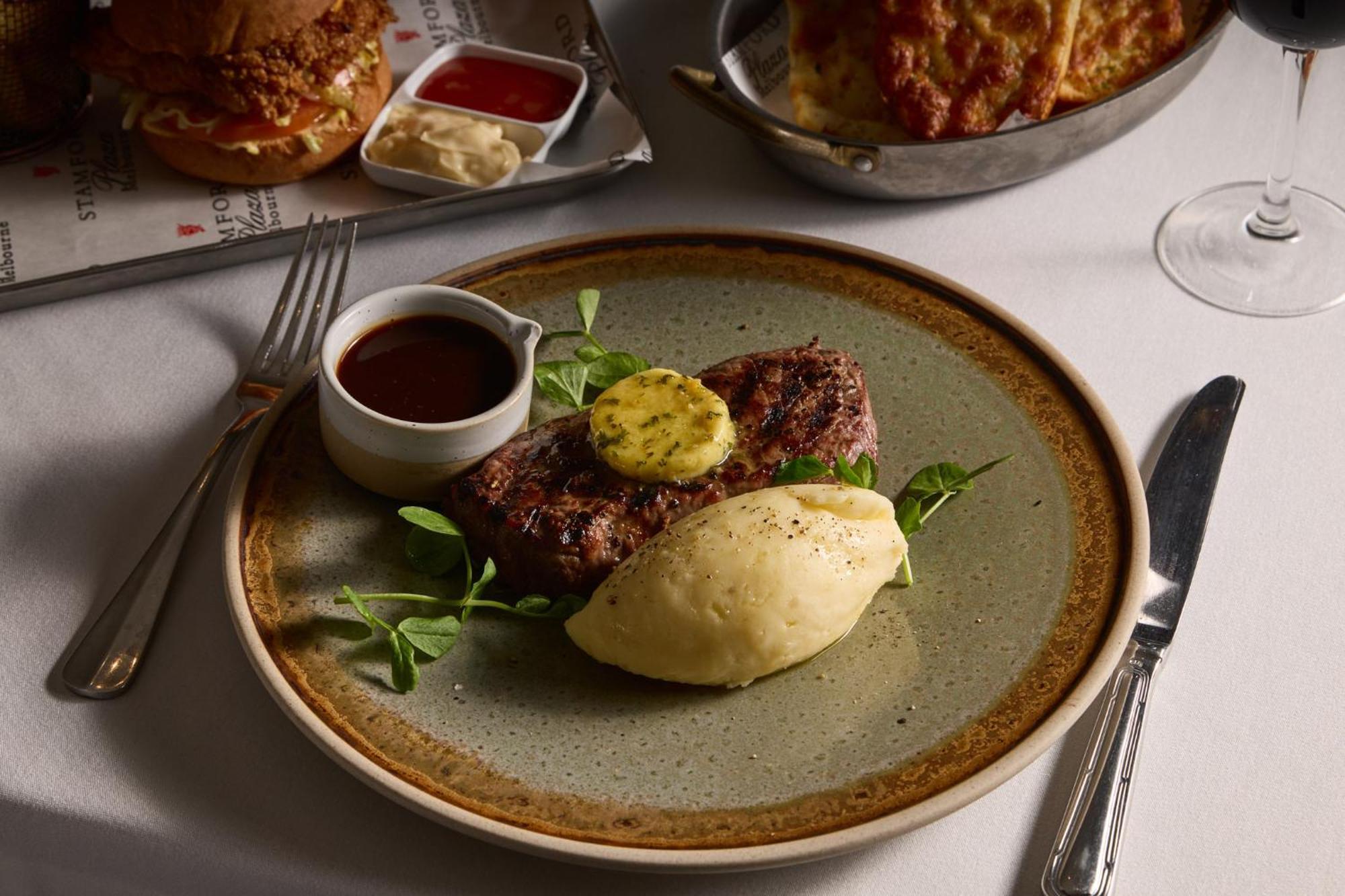 Hotel Stamford Plaza Melbourne Zewnętrze zdjęcie The photo shows a well-presented plate featuring a serving of steak, topped with a dollop of herb butter and surrounded by fresh sprouts or microgreens. There is a smooth portion of mashed potatoes beside the steak, and a small bowl of sauce, likely 