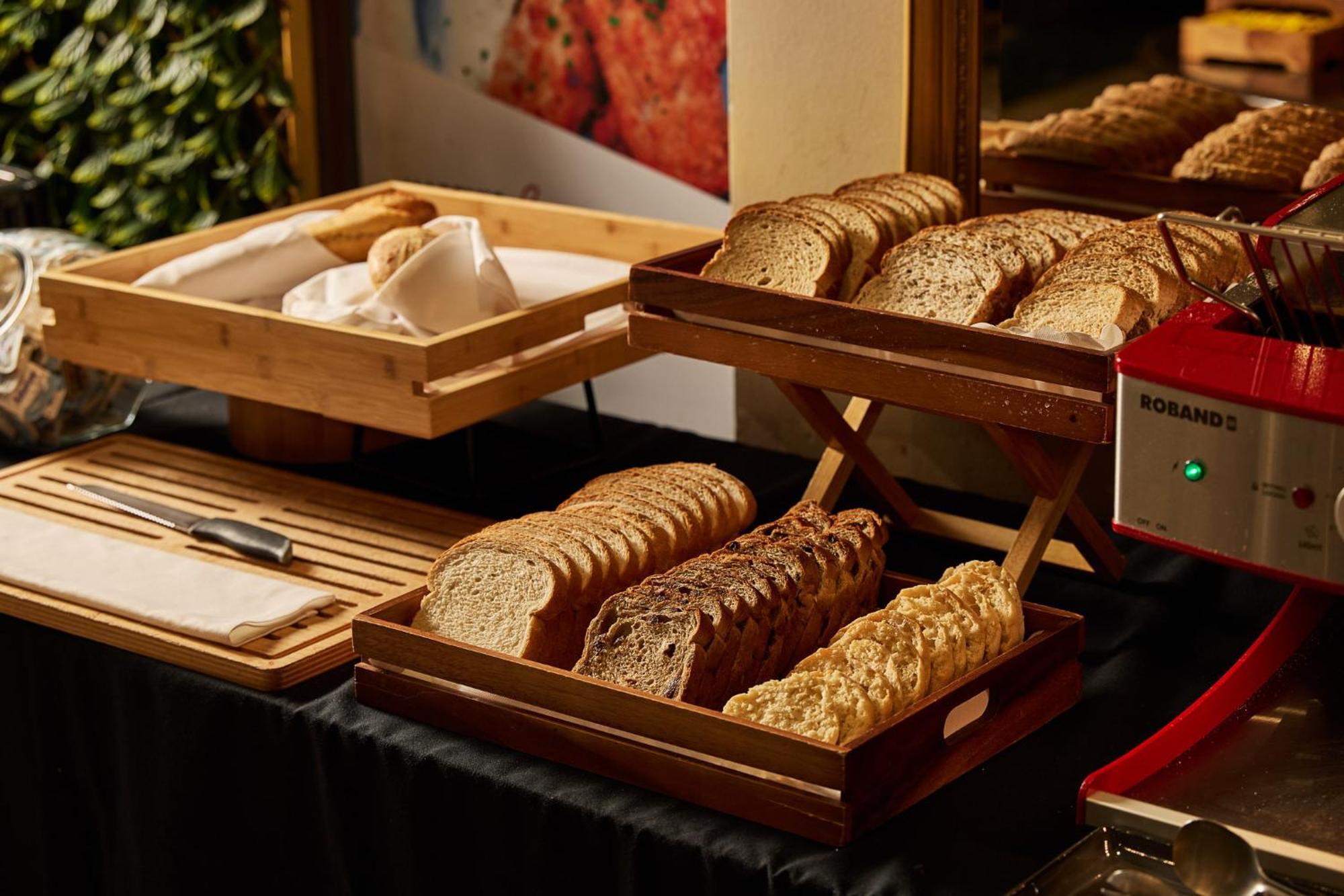 Hotel Stamford Plaza Melbourne Zewnętrze zdjęcie The photo shows a display of various types of bread arranged on wooden trays. There are several stacks of sliced bread, including light and dark varieties. One tray appears to hold a selection of whole grain or multigrain bread, while another feature