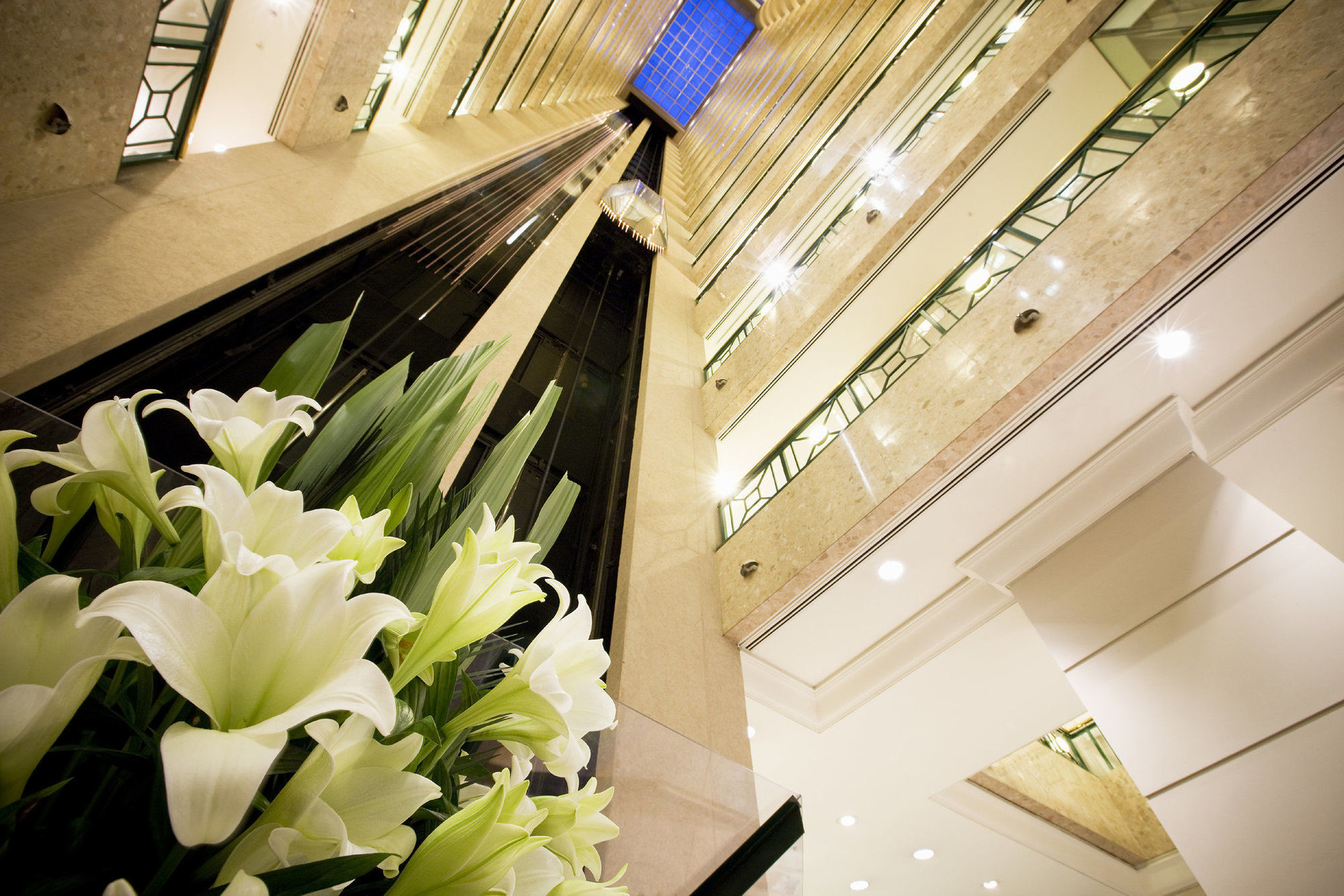 Hotel Stamford Plaza Melbourne Wnętrze zdjęcie The photo shows a modern indoor space, likely a lobby or atrium of a building. The view is looking upwards, capturing a sleek design with multiple levels. There are several elevators in the center, running vertically. The walls are lined with glass a